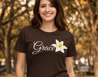 May include: A dark brown t-shirt featuring the word "Grace" in a white script font, accompanied by a white and yellow flower graphic. The shirt is a short-sleeved crew neck.