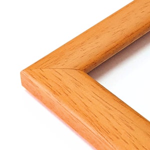 May include: Close-up of the corner of a natural wood picture frame. The frame is a light brown color with a smooth finish.