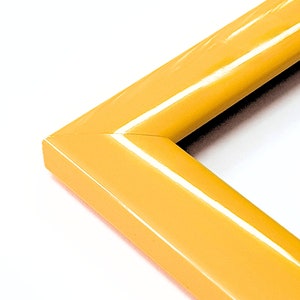 May include: A close-up of the corner of a yellow picture frame. The frame is made of wood and has a glossy finish.