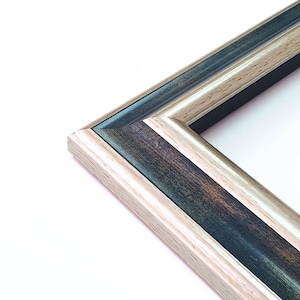 Könnte beinhalten: Nahaufnahme eines Bilderrahmens mit dunkler Holzoptik und einer hellen Holzleiste. Der Rahmen hat eine abgeschrägte Kante und eine dezente goldene Akzent.