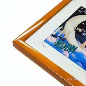 May include: A framed print of a woman flying to the moon. The print is in a yellow frame and has a blue, pink, and white background. The text "Fly Me To The Moon" is written in green letters. The print is numbered 6/200 and signed "Arta Atelier".