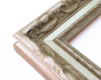 May include: A close-up of a corner of a silver picture frame with an ornate design. The frame has a raised edge and a detailed pattern of leaves and swirls.