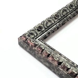 May include: Close-up of a corner of a decorative picture frame. The frame has a detailed, ornate design with a silver and bronze finish. The frame's edges are textured, and the overall style is vintage.