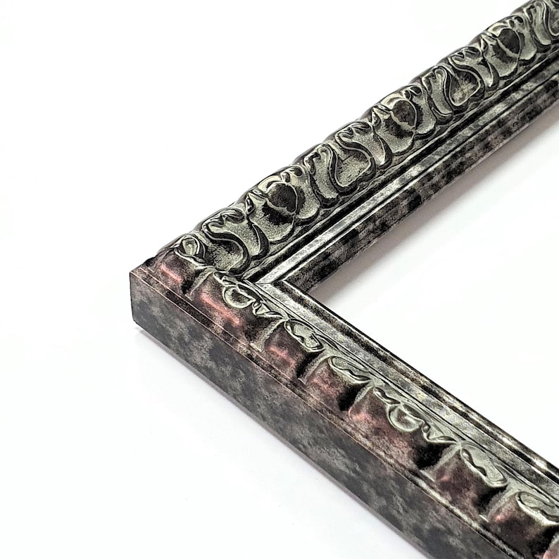 May include: Close-up of a corner of a decorative picture frame. The frame has a detailed, ornate design with a silver and bronze finish. The frame's edges are textured, and the overall style is vintage.