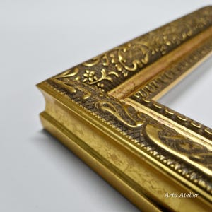 May include: Close-up of a gold picture frame with ornate detailing. The frame has a raised, textured design with a floral pattern. The frame is made of wood and has a gold finish.