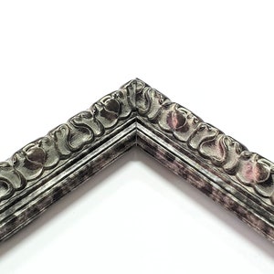 May include: Close-up of a corner of a silver picture frame with an ornate, detailed design. The frame has a distressed, aged look.