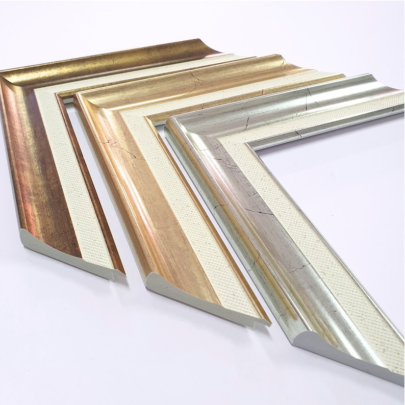 May include: Three picture frames with ornate, decorative edges. The frames are made of wood and have a white, gold, and silver finish. The frames are arranged in a staggered pattern, with the largest frame at the bottom and the smallest frame at the top.