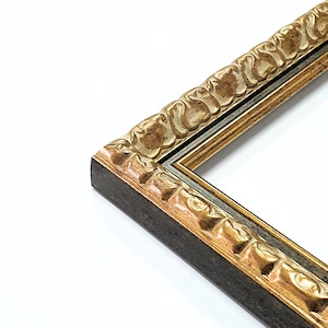 Puede incluir: Primer plano de una esquina de un marco de fotos decorativo. El marco presenta una base marrón oscuro con detalles dorados ornamentados. El diseño del marco incluye un patrón floral tallado a lo largo de los bordes, creando una estética vintage.