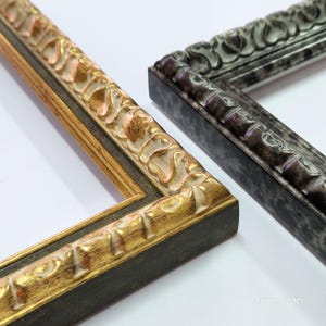 May include: Close-up of two ornate picture frame corners. One frame has a gold and brown finish with detailed floral carvings. The other frame has a dark gray and silver finish with similar carvings. Both frames are on a white background.