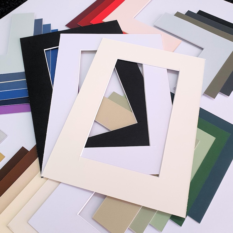 May include: Assortment of colored mat boards with different sized openings for framing artwork or photos. The mat boards are in various shades of green, blue, red, brown, and beige.