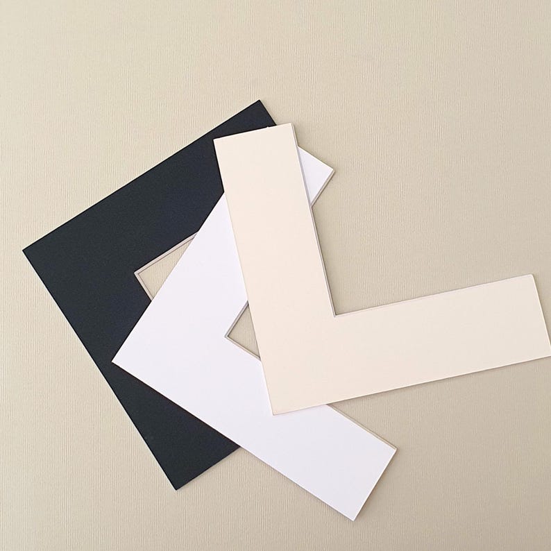 May include: Three mat boards in different colors: black, white, and cream. The boards are cut in a standard mat board shape with a window opening in the center.