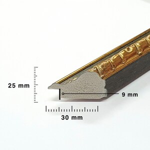 May include: Close-up of a decorative picture frame molding. The frame has a gold-colored ornate design on the top edge, with a dark gray base. The frame is 30 mm wide, 25 mm high, and 9 mm thick.