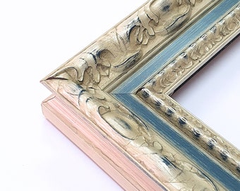 May include: Close-up of a decorative picture frame corner. The frame has ornate carvings in a distressed gold finish, with a light blue and pink accent. The frame is designed for displaying artwork or photographs.