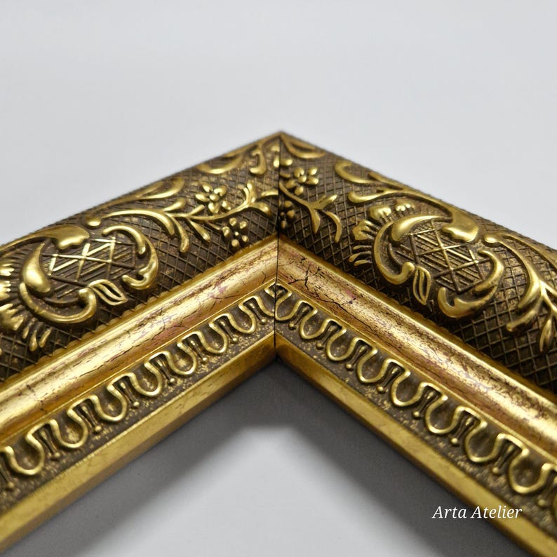 May include: Close-up of a gold picture frame with an ornate design. The frame has a raised, textured pattern with a floral motif. The frame is made of wood and has a gold finish.