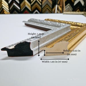 May include: Close-up of a silver and gold picture frame with ornate details. The frame is 1.85 inches wide and 1.42 inches high. The rebate is 0.63 inches.