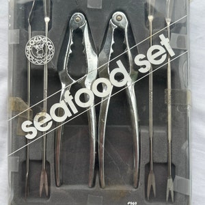 May include: A vintage seafood set in a clear plastic case. The set includes two chrome-plated nutcrackers, four slender tools, and the words "Seafood Set" in white. The case is marked with the number #969.