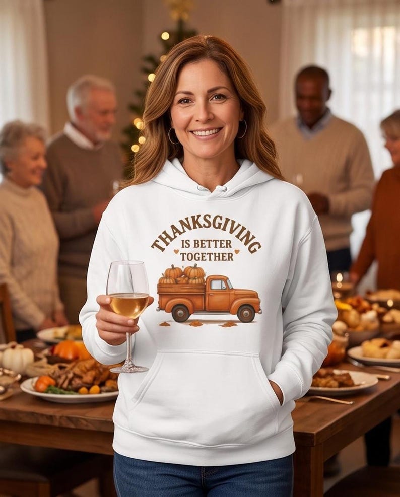 A woman wearing a white hoodie with a Thanksgiving truck graphic holds a glass of white wine at a family dinner setting.