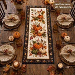May include: A rectangular table runner with a quilted white center featuring a printed design of pumpkins, autumn leaves, and sunflowers, bordered by a dark navy blue frame with floral patterns. Text on the image reads: PRINTED DESIGN – NOT EMBROIDERED.
