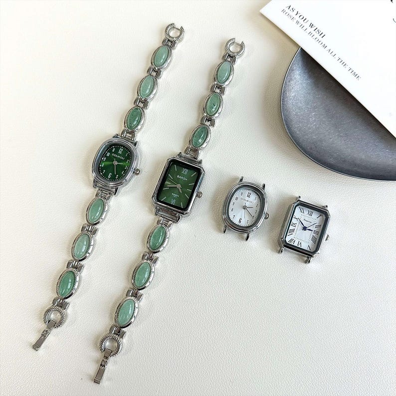 May include: Several silver-toned watches with different face shapes and green or white dials. Two watches have green oval-shaped stones on the bands. One watch has a rectangular face with the word "BANSH" on the dial. The other watches have white dials.