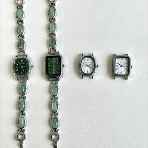 May include: Four watches with silver-toned metal cases. Two have green watch faces and matching green stone bands. The other two have white watch faces. One has a rectangular face with Roman numerals, and the other has an oval face with Arabic numerals.