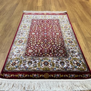 May include: A red and white patterned rug with a fringe border. The rug has a floral design and is made of a soft, plush material.