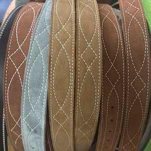 Peut inclure: Une collection de ceintures en cuir de différentes nuances de marron, de gris et de vert. Chaque ceinture présente un motif décoratif cousu en fil blanc. Les ceintures sont disposées en rang, mettant en valeur leurs différentes couleurs et leurs motifs.
