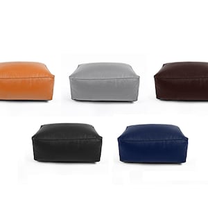 May include: Five square ottomans in tan, grey, dark brown, black, and navy blue. Each has a smooth, leather-like texture and a low profile, suitable for seating or footrests. Each ottoman is approximately 60cm x 60cm.