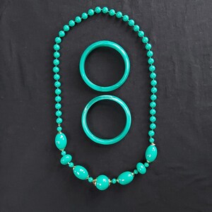 Può includere: Un set di gioielli composto da una collana lunga e due braccialetti abbinati. La collana presenta piccole perline rotonde color turchese, perline ovali più grandi e distanziatori metallici. I due braccialetti circolari sono in materiale turchese liscio.