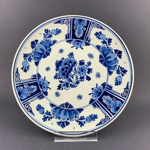 May include: A white ceramic plate with a blue and white floral design. The plate has a raised rim and a scalloped edge. The floral design is intricate and features a variety of flowers and leaves.