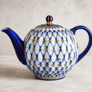 Könnte beinhalten: Eine Teekanne aus Porzellan mit weißem Körper und einem blau-goldenen Gittermuster. Die Teekanne hat einen tiefblauen Henkel, einen passenden blauen Ausguss und einen Deckel mit blau-goldener Verzierung. Das Design enthält kleine goldene Akzente an jeder Kreuzung der blauen Gitterlinien, was dieser Teekanne ein detailliertes und verziertes Aussehen verleiht.