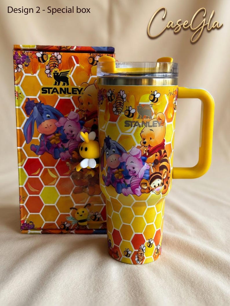 May include: Yellow Stanley tumbler and matching box featuring a honeycomb pattern and images of Winnie the Pooh and friends. The tumbler has a yellow handle and lid, with the Stanley logo visible. The box reads "Design 2 - Special box".