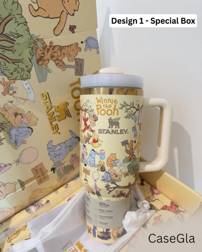 May include: A yellow Stanley tumbler featuring Winnie the Pooh characters. The tumbler has a cream-colored handle and lid, with the text "Winnie the Pooh" and "Stanley" printed on it. The tumbler is in a matching box with character illustrations.