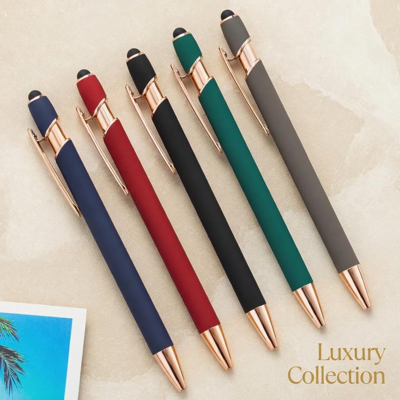 May include: Six pens in a row, each with a different color barrel: navy, red, black, green, and gray. The pens have gold-colored accents and a black stylus tip. The text "Luxury Collection" is in the bottom right corner.
