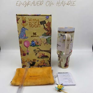May include: A Winnie the Pooh themed gift set featuring a tumbler, box, straw, and accessories. The tumbler and box have illustrations of Pooh and friends. The set includes a yellow pouch and a bee-shaped charm.