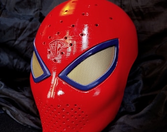 Puede incluir: Una máscara facial completa de color rojo brillante con una serie de pequeños orificios de ventilación en la frente y la barbilla. La máscara incluye dos aberturas para los ojos enmarcadas en azul oscuro con malla dorada y un logo.