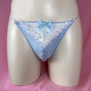 May include: Light blue thong underwear with white lace trim and a satin bow. The bow is centered on the front and has a small pearl in the center. The underwear has a delicate, feminine design.