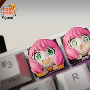 May include: Four pink and white anime-style keycaps with different facial expressions. The keycaps are on a white keyboard with black keys.
