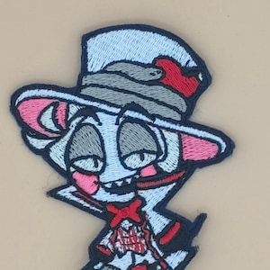 Peut inclure: Patch brodé thermocollant représentant un personnage de dessin animé portant un haut-de-forme, un nœud papillon et un cœur rouge sur le chapeau. Le personnage a un visage blanc, des yeux gris et des oreilles roses. Le patch est sur un fond beige.
