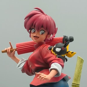 Puede incluir: Una figura de personaje de anime con cabello rojo que lleva una camisa roja y pantalones azules. El personaje sostiene un paraguas rojo y tiene una criatura negra y amarilla en su hombro.
