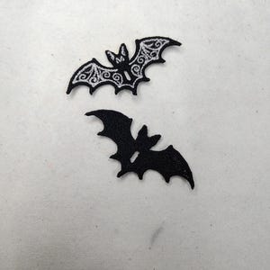 Può includere: Due toppe nere a forma di pipistrello. Un pipistrello ha un design bianco e ornato sulle ali e sul corpo. L'altro pipistrello è una silhouette nera piena. Adatto per lavori artigianali a tema Halloween o gotico.