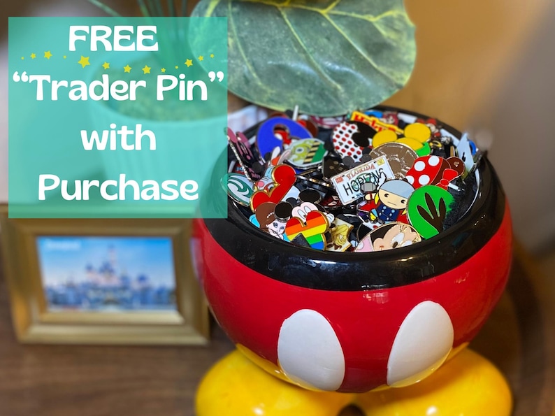May include: A red, black, and white Mickey Mouse-themed bowl overflowing with colorful enamel pins. The pins feature various designs and characters. Text in the image reads "FREE Trader Pin with Purchase."