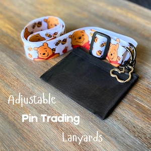 May include: White lanyard with a repeating pattern of Winnie the Pooh and bees. Includes a black cardholder and a Mickey Mouse-shaped keychain. The text "Adjustable Pin Trading Lanyards" is printed on the image.