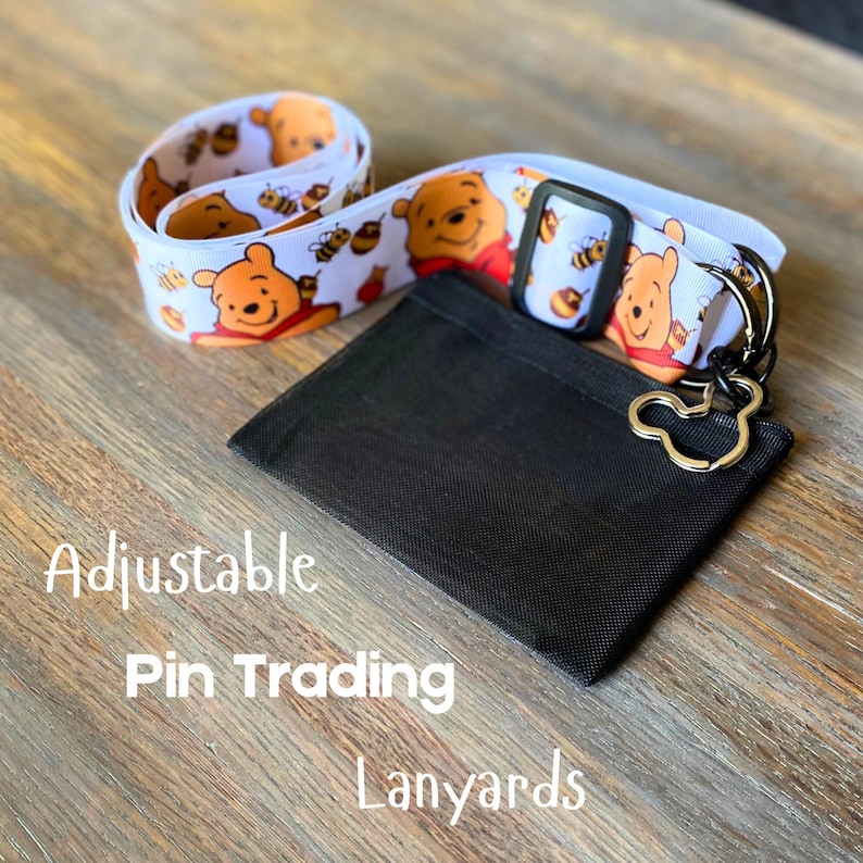 May include: White lanyard with a repeating pattern of Winnie the Pooh and bees. Includes a black cardholder and a Mickey Mouse-shaped keychain. The text "Adjustable Pin Trading Lanyards" is printed on the image.