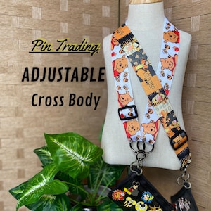 May include: Adjustable cross-body lanyard with a Winnie the Pooh theme. The lanyard features a repeating pattern of Winnie the Pooh, bees, and Tigger. The text "Pin Trading" and "ADJUSTABLE Cross Body" are visible in the image.