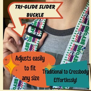 May include: A black tri-glide slider buckle on a white strap with the text "Beyond" and colorful geometric patterns. The strap is designed to adjust easily to fit any size, from traditional to crossbody.