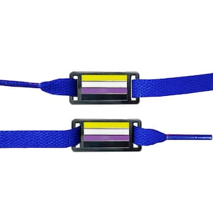Peut inclure: Deux breloques de lacets bleus avec un cadre métallique et un motif de drapeau jaune, blanc, violet et noir. Le drapeau est le drapeau de la fierté non binaire.
