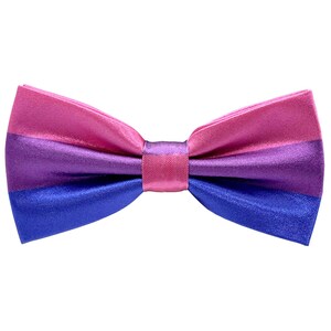 Pode incluir: Uma gravata borboleta listrada em rosa, roxo e azul. A gravata borboleta é feita de cetim e tem um formato clássico.