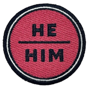 May include: A red circular patch with a white border and black text that reads "HE HIM".