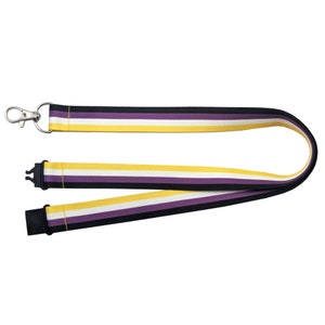 Może przedstawiać: Smycz z paskiem w kolorze fioletowym, białym i żółtym. Smycz ma srebrny klips na jednym końcu i czarny klips na drugim końcu.