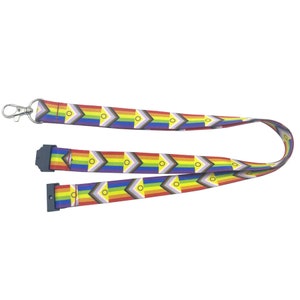 Op de afbeelding: Een regenboog-koord met een herhalend patroon van een regenboogvlag met een gele cirkel in het midden. Het koord heeft een zilveren draaibare clip en een zwarte plastic veiligheidsklem.